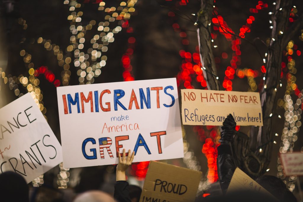 hands holding protest signs reading immigrants make america great