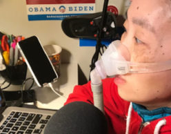 [Image Description: Photo of an Asian American woman at a desk. She is looking at her laptop computer and there is a microphone in front of her. She has headphones over her ears and is wearing a mask over her nose attached to a gray tube.] Photo Courtesy of Alice Wong